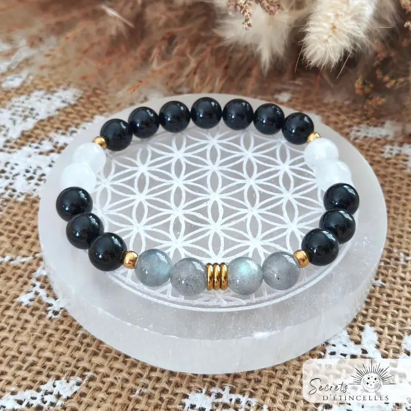 bracelet protection en pierres naturelles de lithothérapie finition dorée, posé sur une fleur de vie, pierres : tourmaline noire, labradorite, selenite